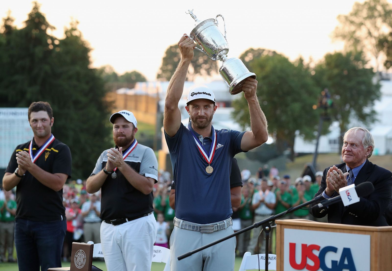 Johnson levanta el trofeo del US Open aplaudido por el ganador de los aficionados, Jon Rahm (izquierda)