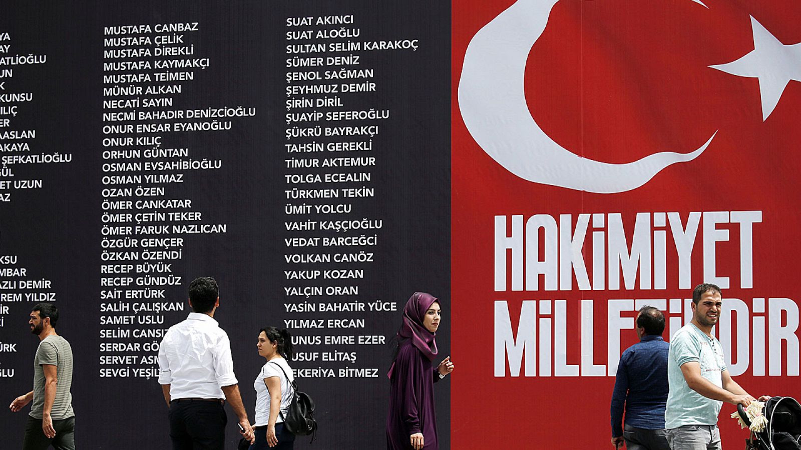 Turcos caminan junto a un gran mural que recoge los nombres de los civiles y policías asesinados durante el intento de golpe de Estado contra Erdogan.
