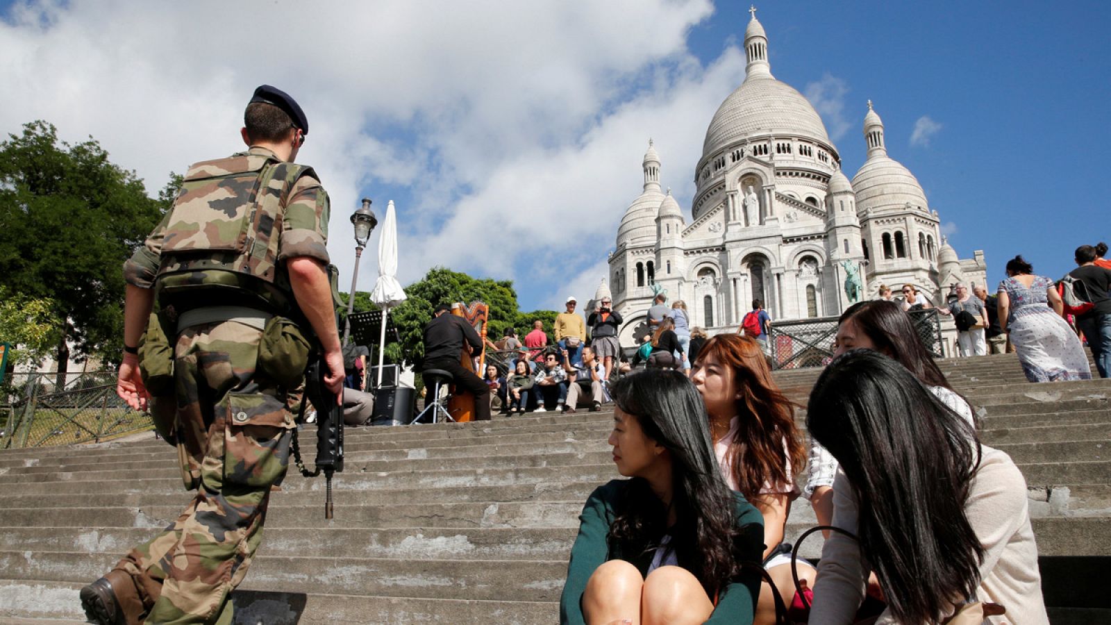 Un soldado patrulla en la basílica del Sagrado Corazón de Montmartre, París, bajo la curiosa mirada de un grupo de turistas coreanas