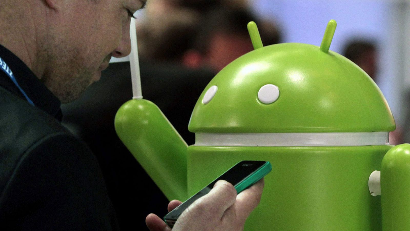 Un hombre consulta un móvil junto al logo de Android, el sistema operativo de Google