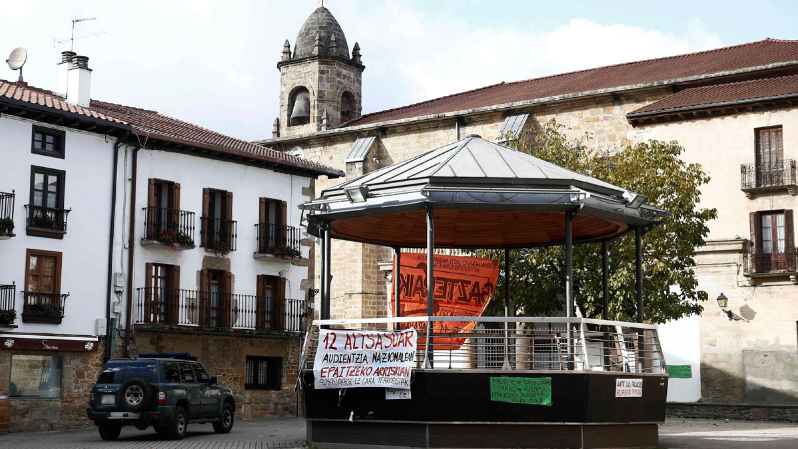 Un vehículo de la Guardia Civil pasa junto al kiosko de la Plaza de Alsasua donde se han colocado varias pancartas tras las detenciones que se han producido este lunes.