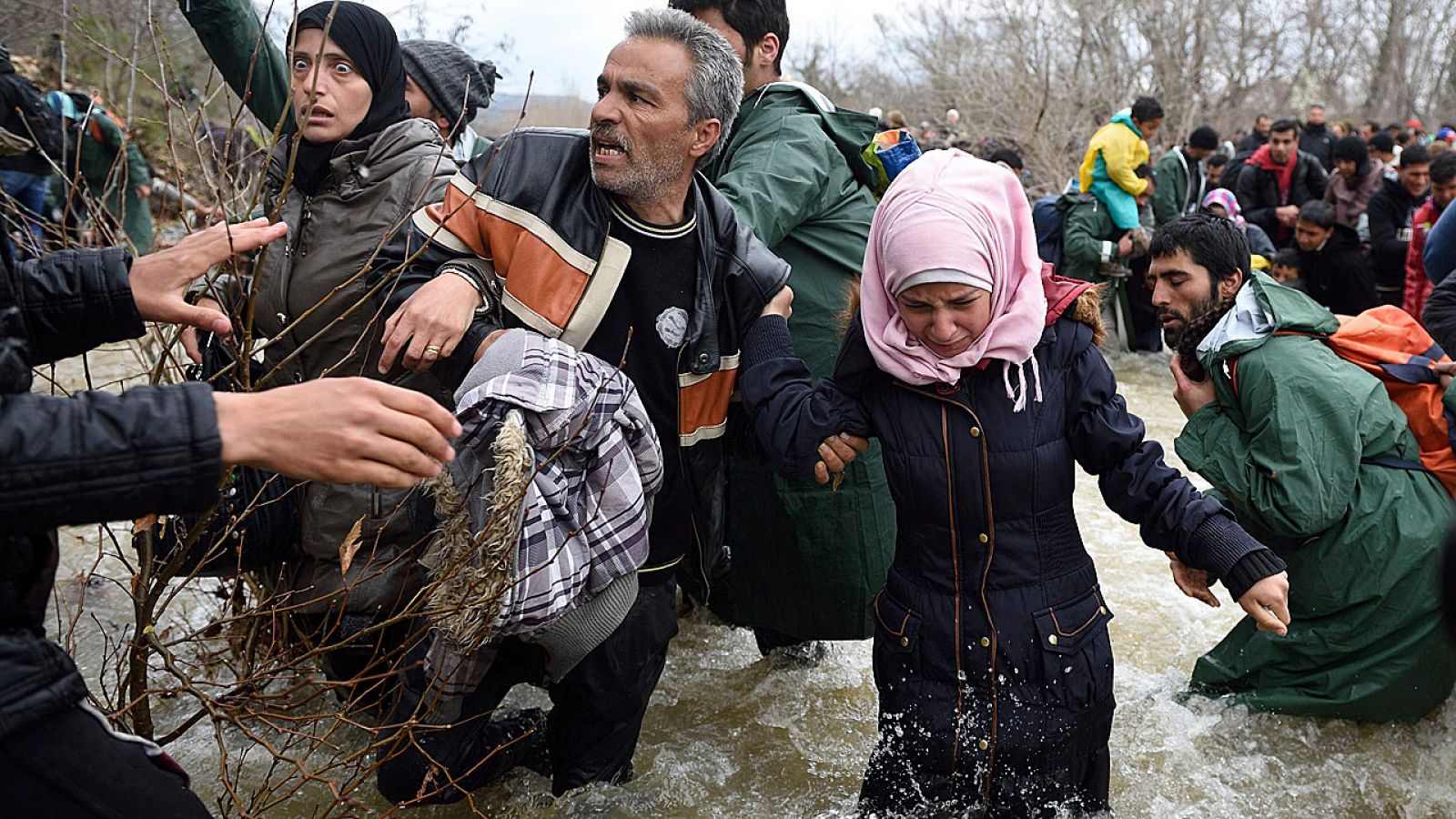 Refugiados y migrantes intentan cruzar un río en la frontera entre Grecia y Macedonia.