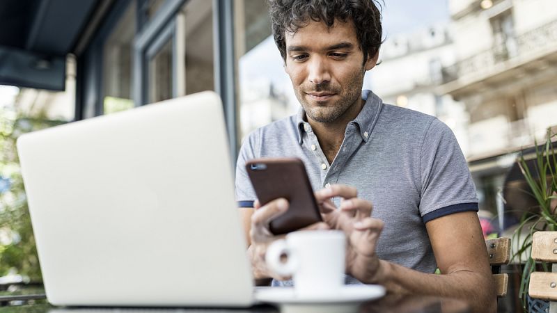 Un hombre trabaja con su ordenador y su teléfono móvil desde una cafetería.