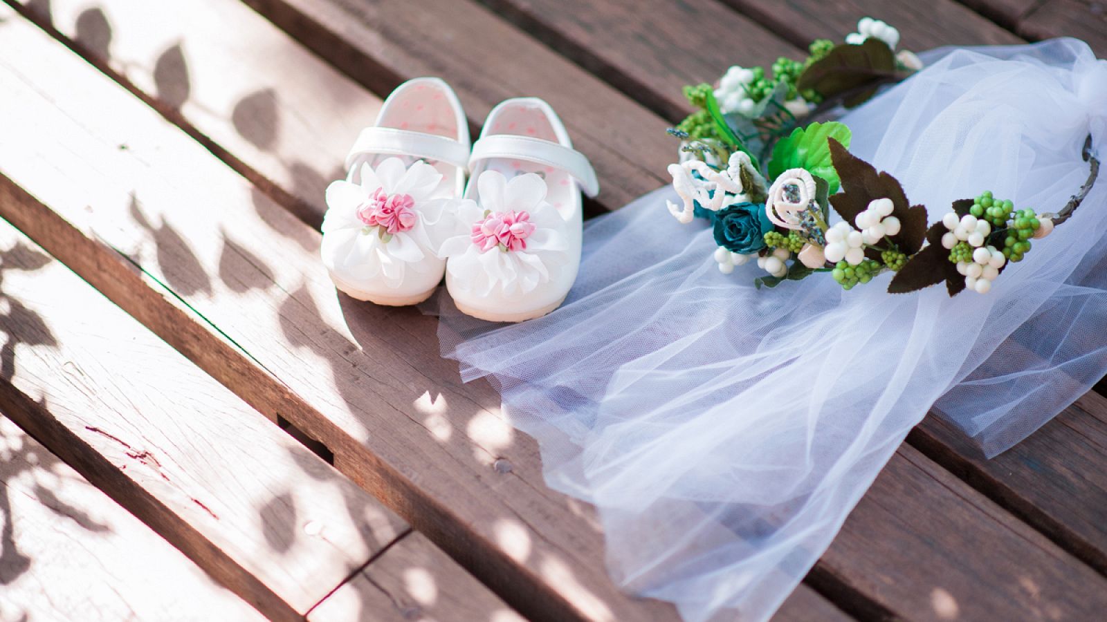 Imagen de unos zapatos de niña junto a un velo y una corona de flores