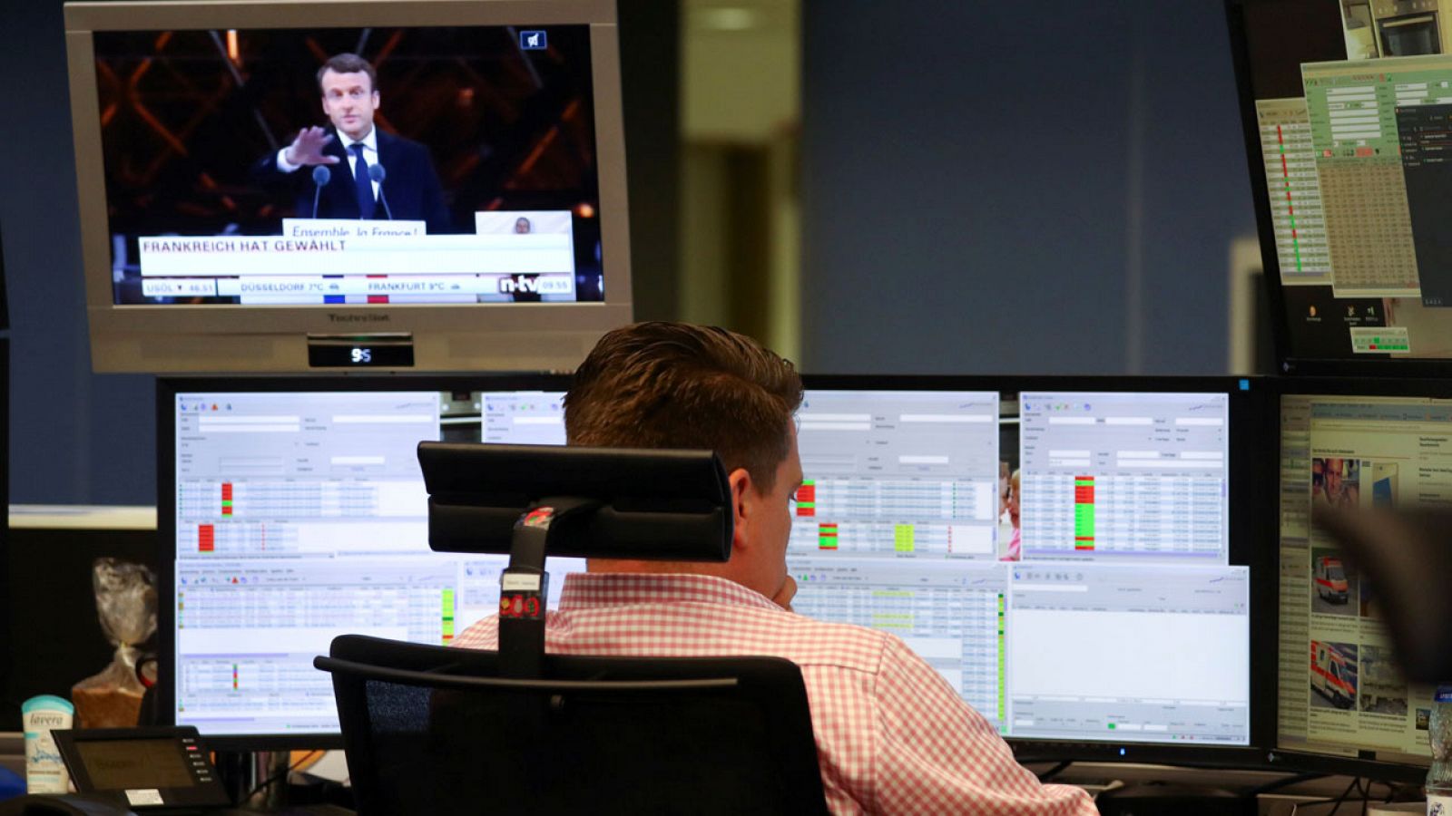 Un empleado trabaja en la Bolsa de Fráncfort mientras Macron aparece en un televisor