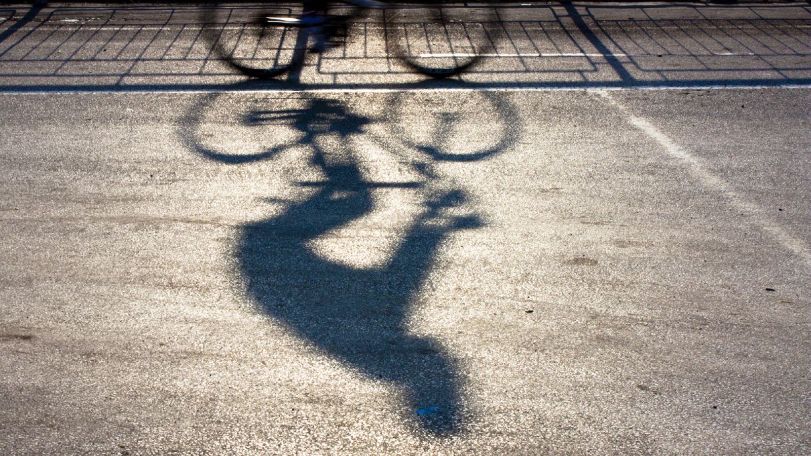 La sombra de un ciclista se proyecta en una carretera.