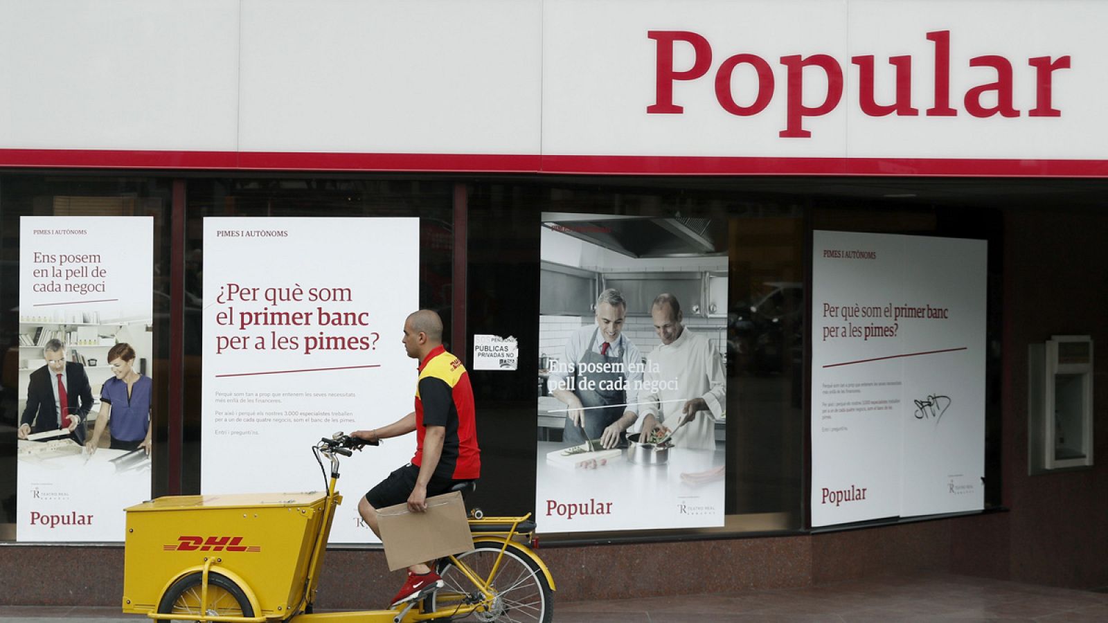 Un repartidor pasa frente a una sucursal del Popular en Barcelona