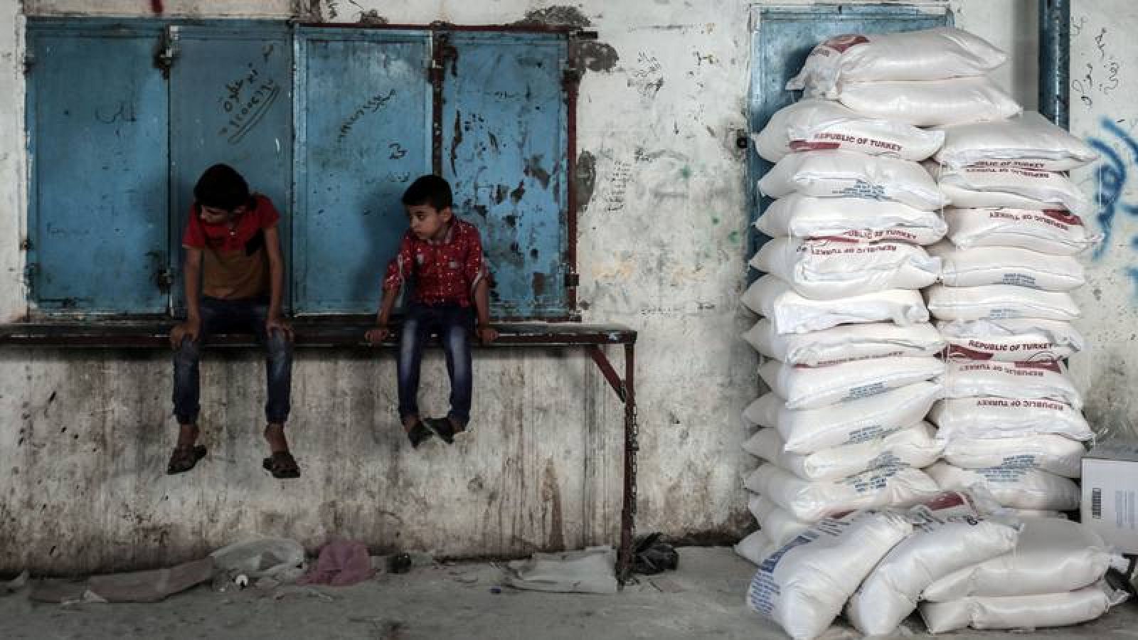  Dos niños gazatíes esperan sentados al lado de sacos de comida provenientes de la ayuda humanitaria de Agencia de Naciones Unidas para los Refugiados de Palestina en Oriente Próximo.