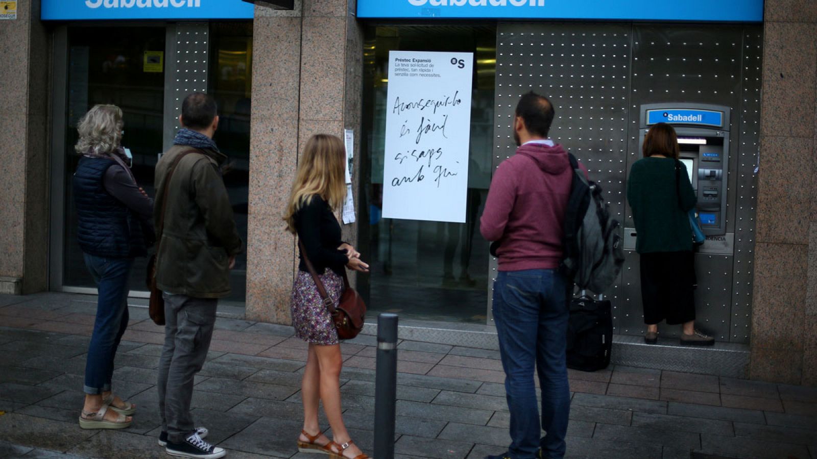 Varias personas esperan ante el cajero de una oficina del Banco Sabadell en Barcelona, como parte de la acción de protesta puesta en marcha por ANC y Òmnium Cultural