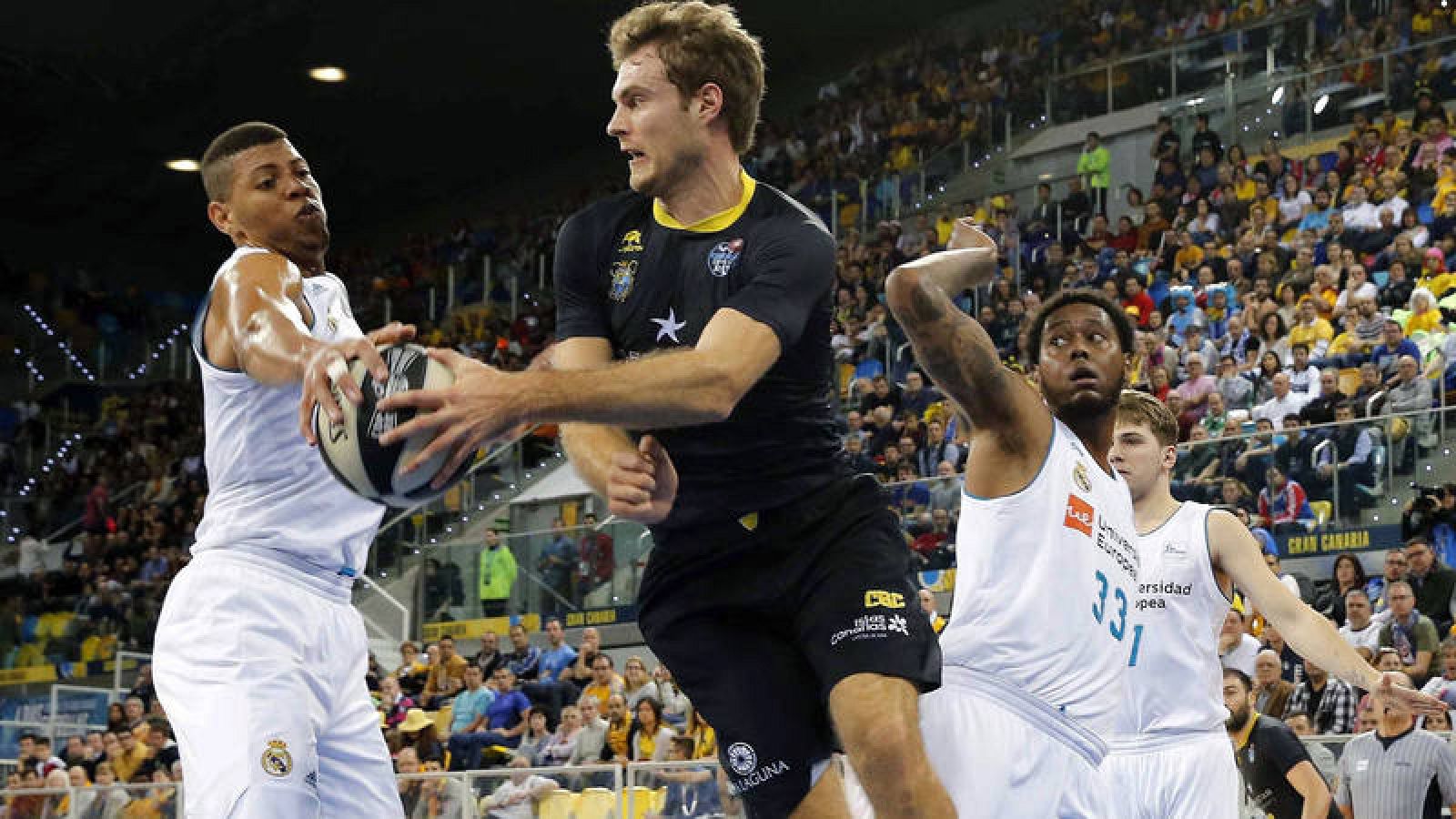 El ala pívot norteamericano del Iberostar Tenerife Tim Abromaitis supera a los jugadores del Real Madrid Edy Tavares (i) y Trey Thompkins (d).