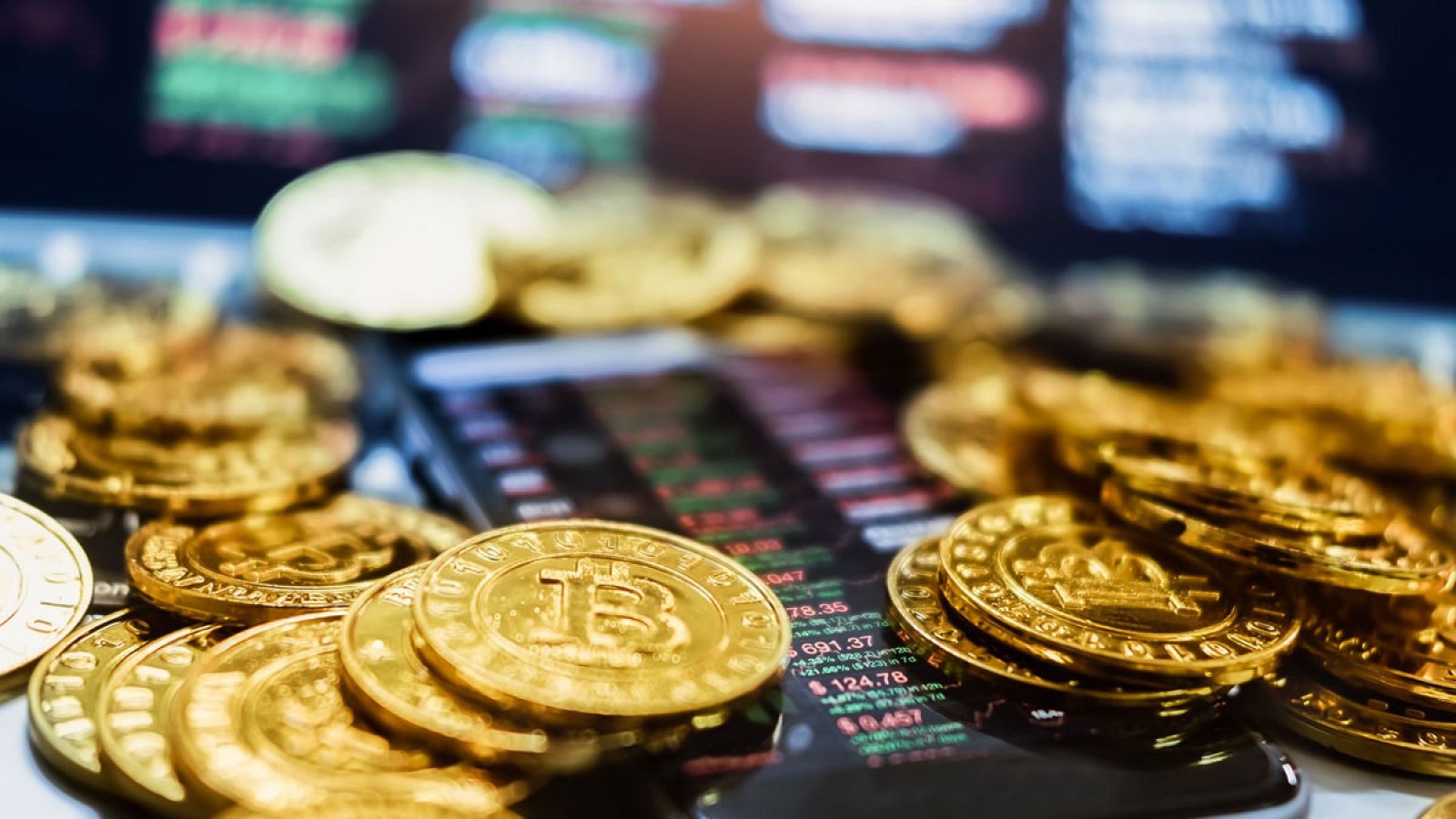 Monedas representando bitcoins junto a un móvil con datos bursátiles