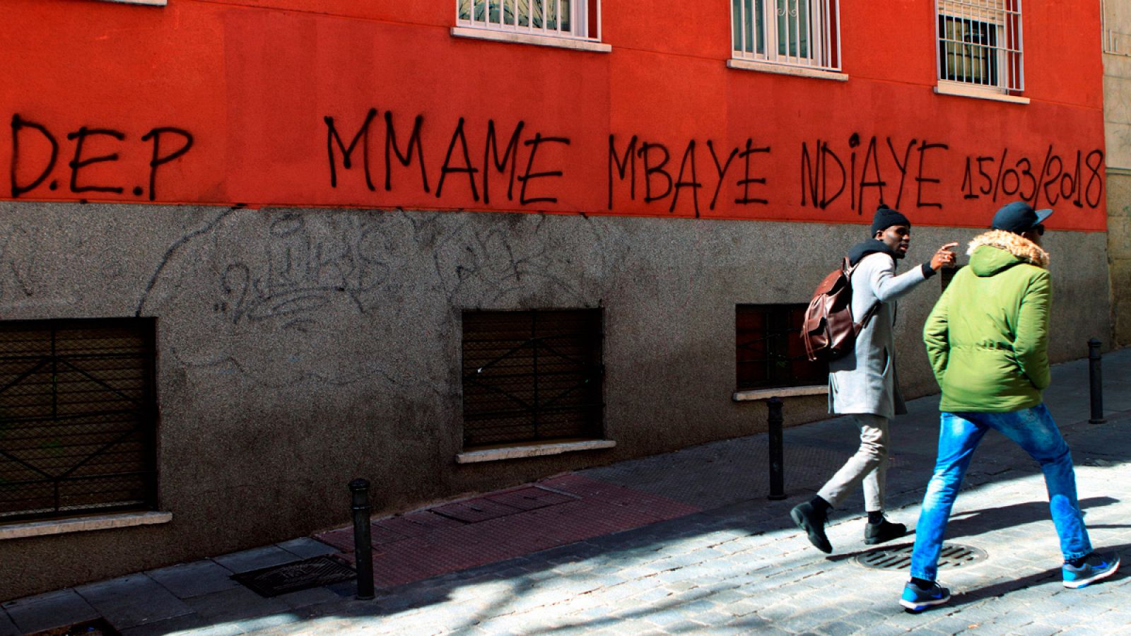 Dos personas pasan delante de una pintada en el madrileño barrio de Lavapiés, en memoria del senegalés que murió de un infarto en plena calle.