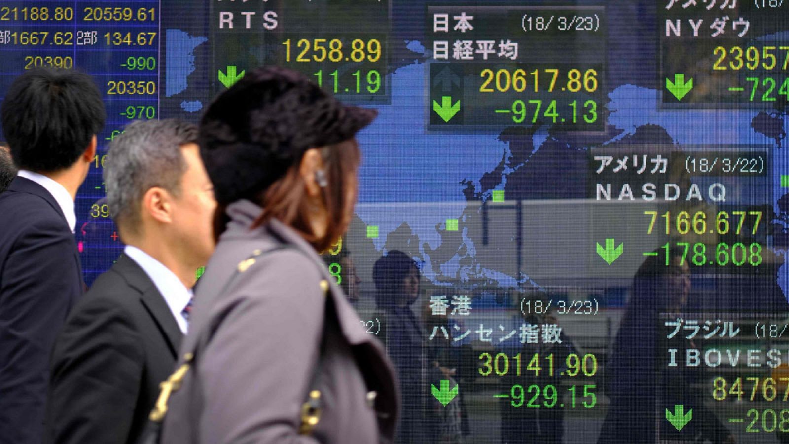 Varios transeúntes pasan delante de un escaparate en Tokio con monitores de los principales índices bursátiles