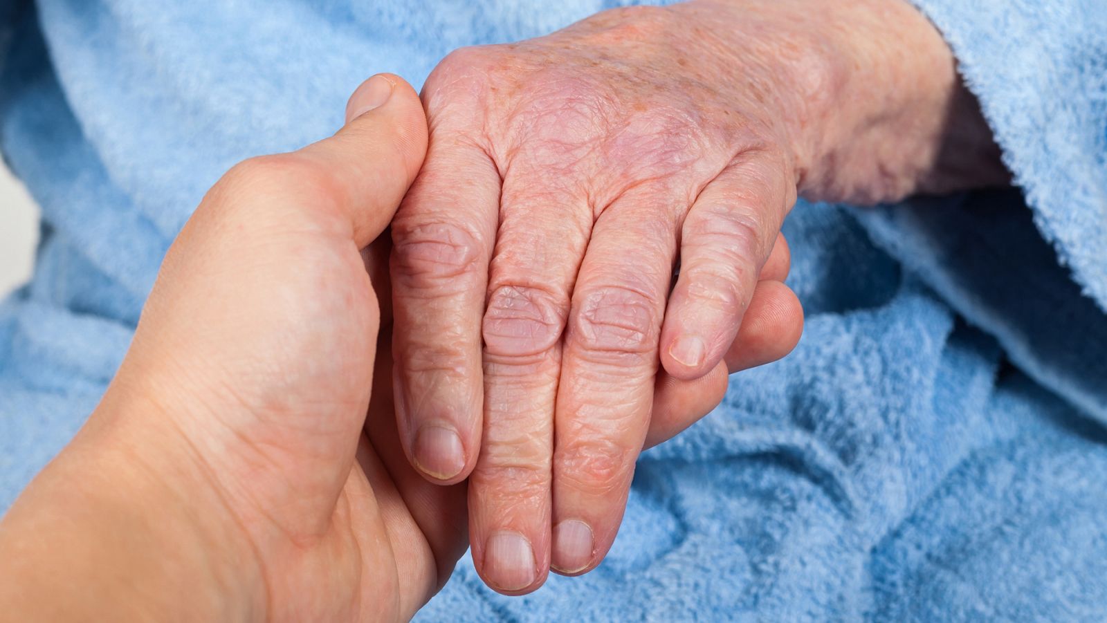 Imagen de recurso: un hombre sostiene la mano de una mujer anciana