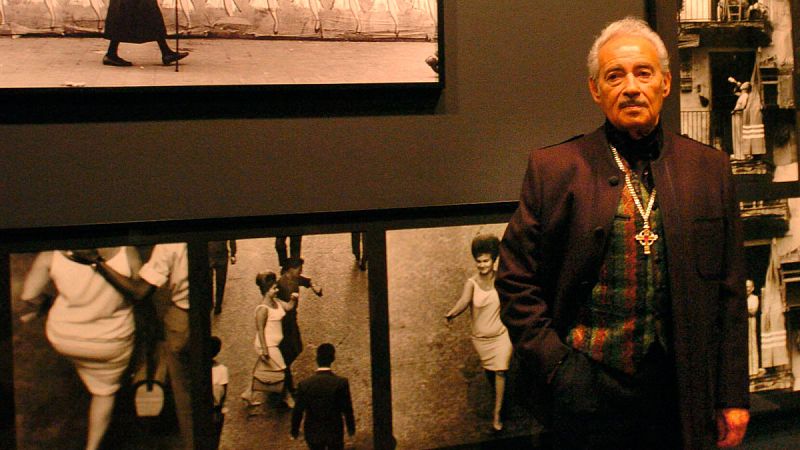 El fotógrafo Eugeni Forcano posando junto algunos de sus trabajos que formaron parte de la exposición Eugeni Forcano. 1960-1996