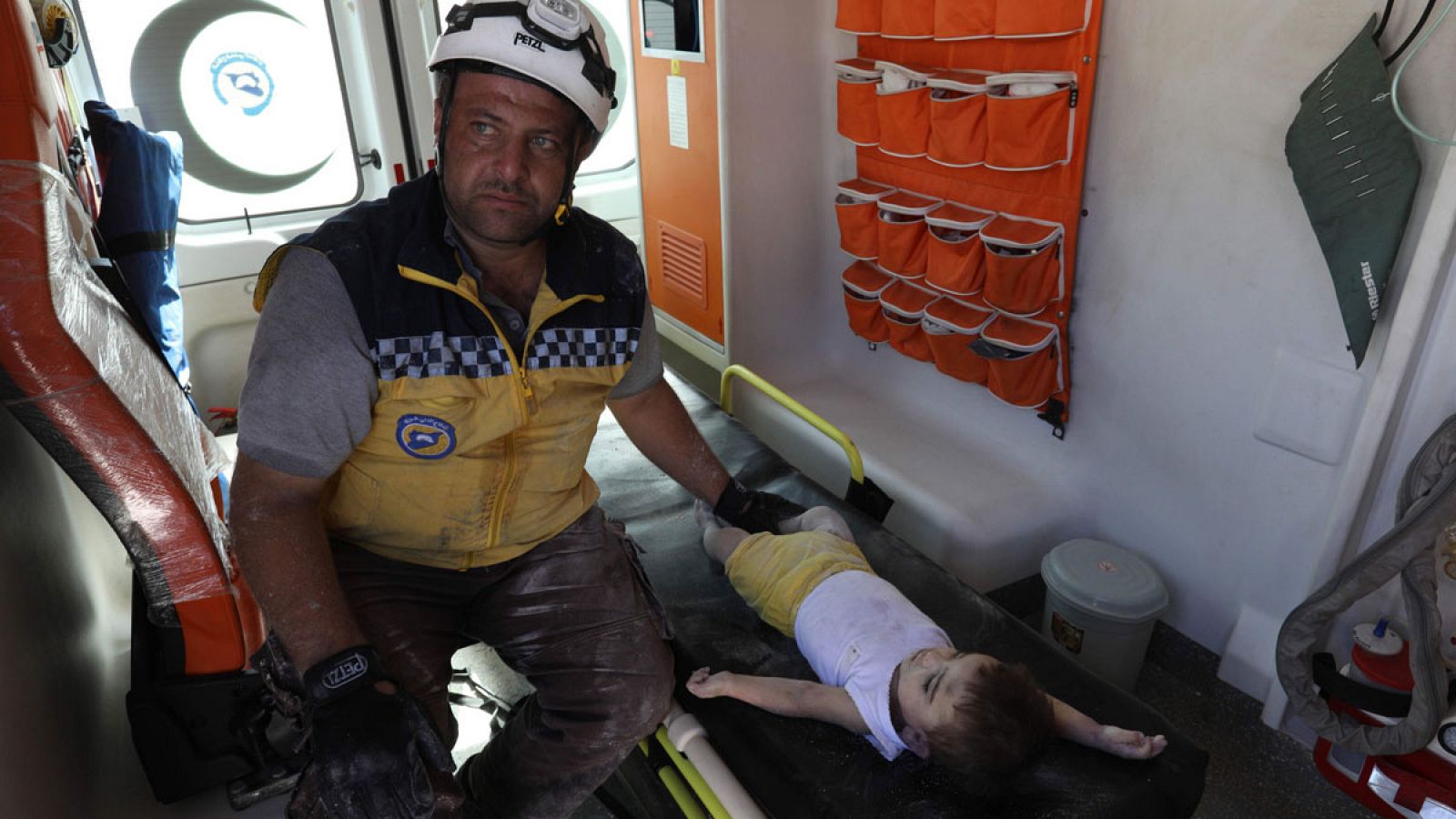 Un miembro de los equipos de rescate junto a un niño tras la explosión en un almacén de municiones en Siria