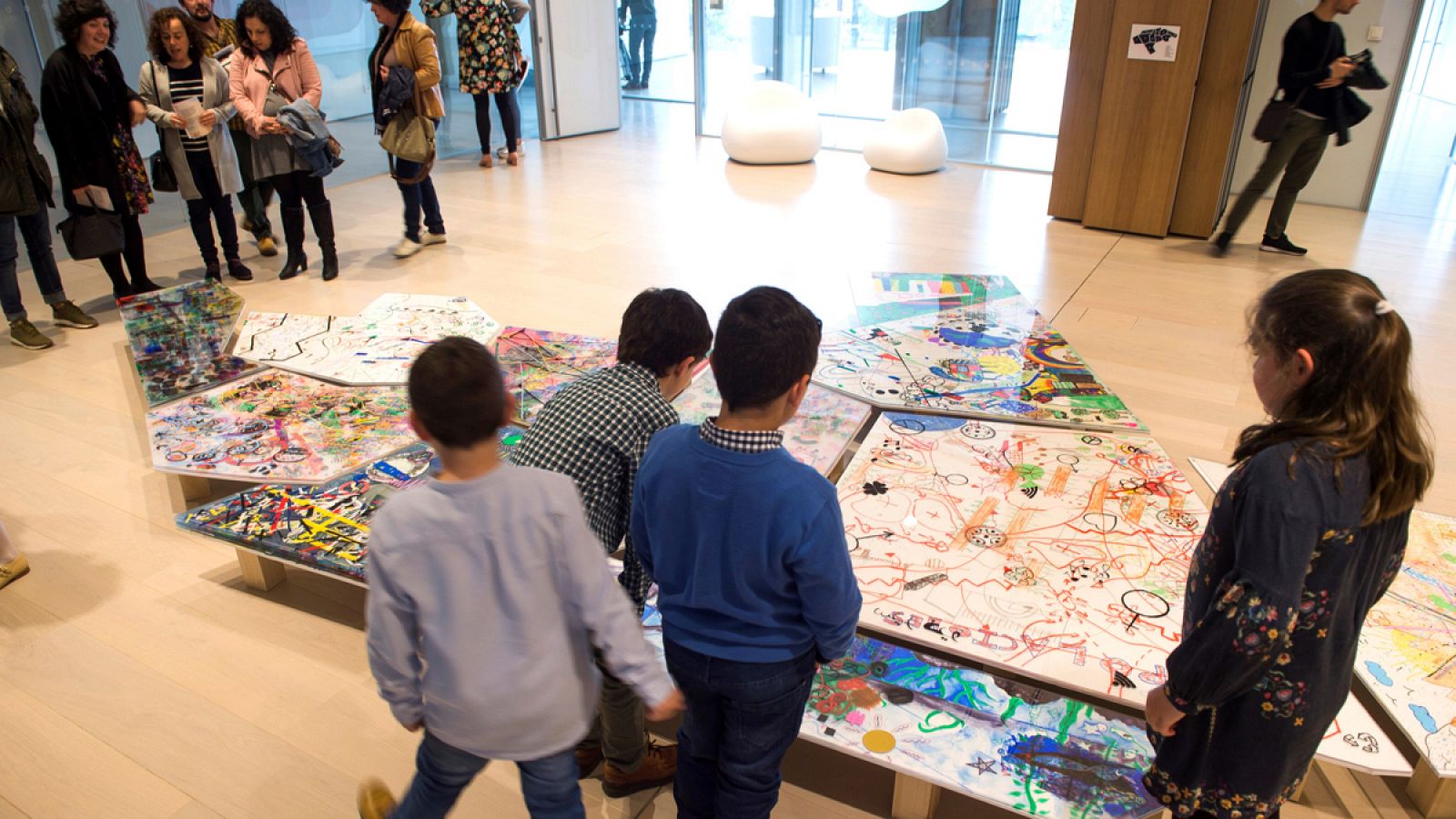 Unos niños observan una obra de arte bajo la mirada de sus cuidadoras.