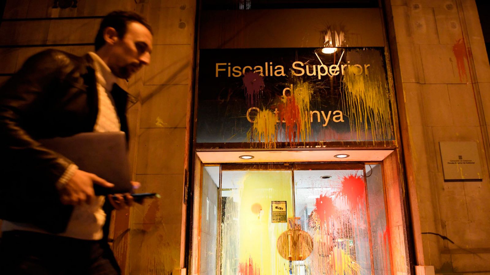 Un hombre caminando frente a la sede de la Fiscalía del Tribunal Superior de Justicia de Cataluña en la que se aprecia las manchas de pintura lanzada por miembros de Arran y de los CDR.
