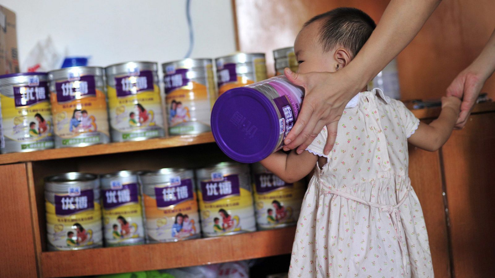 Imagen de una niña sosteniendo una lata de leche infantil en polvo.