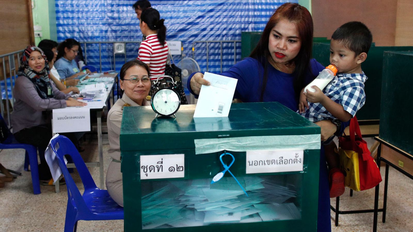 Una mujer con un niño en brazos deposita su voto en la urna durante las elecciones anticipadas de este lunes