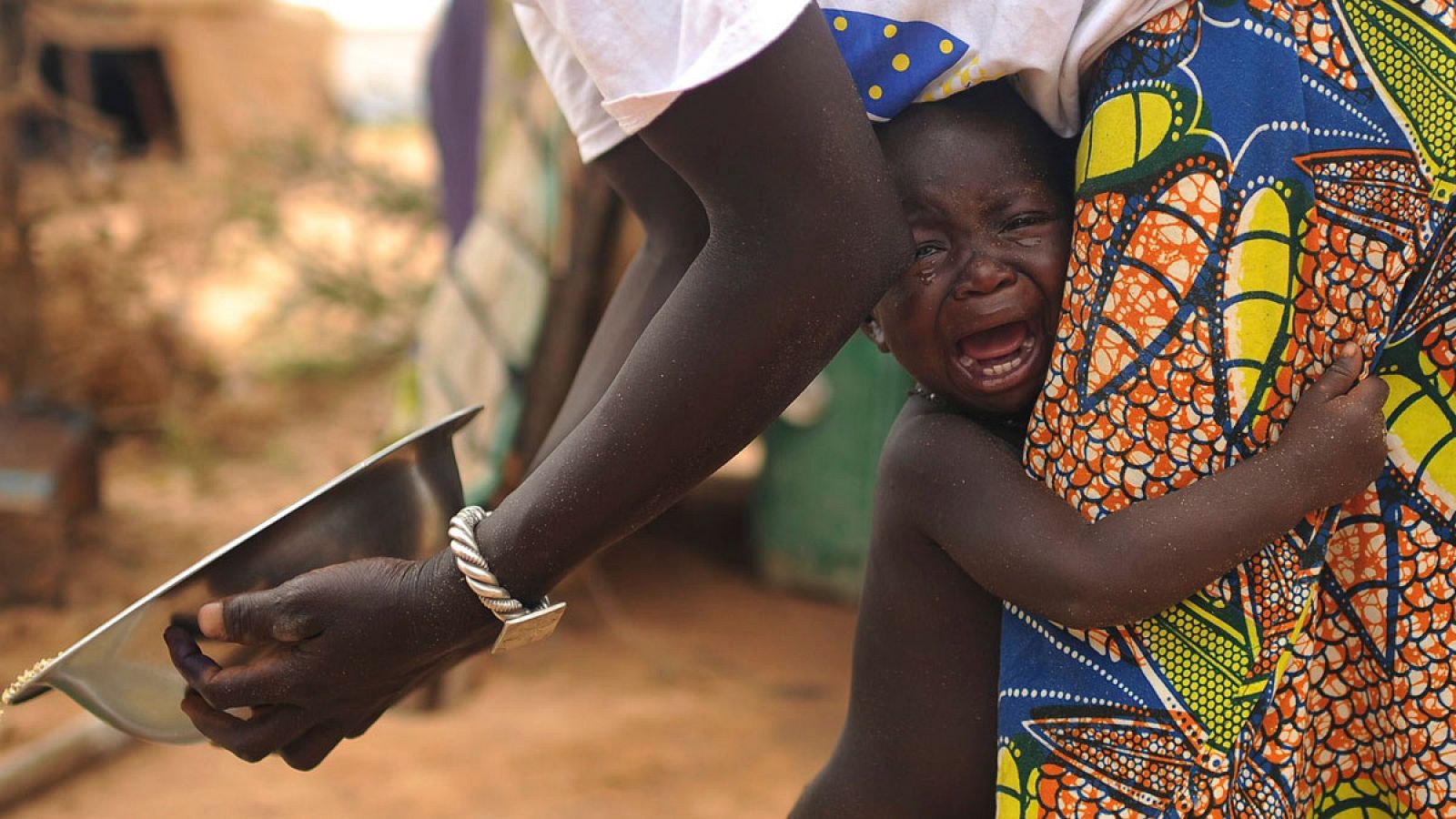 Una mujer con atuendo africano consuela en su regazo a un niño llorando.