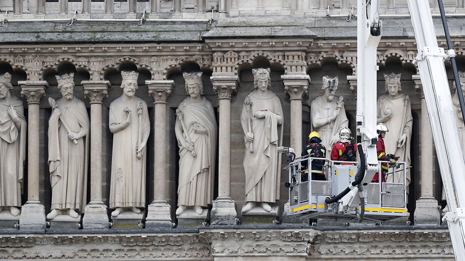Varios bomberos trabajan en un elevador junto a varias esculturas de la fachada de Notre Dame