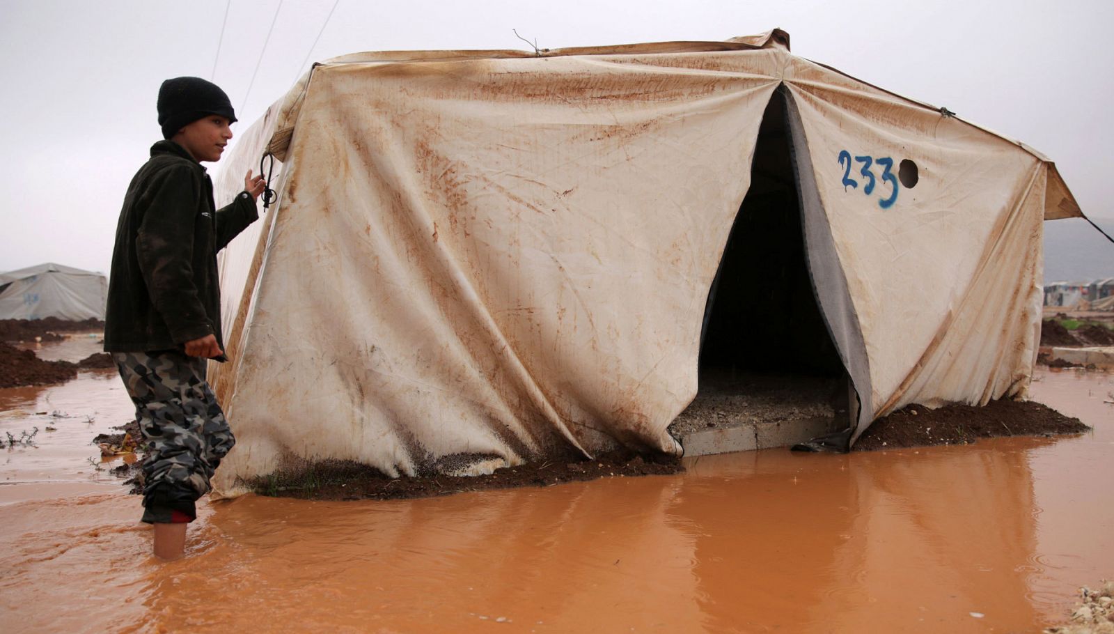 Un chico sirio camina cerca de la tienda de campaña inundada en el campo de refugiados donde vive