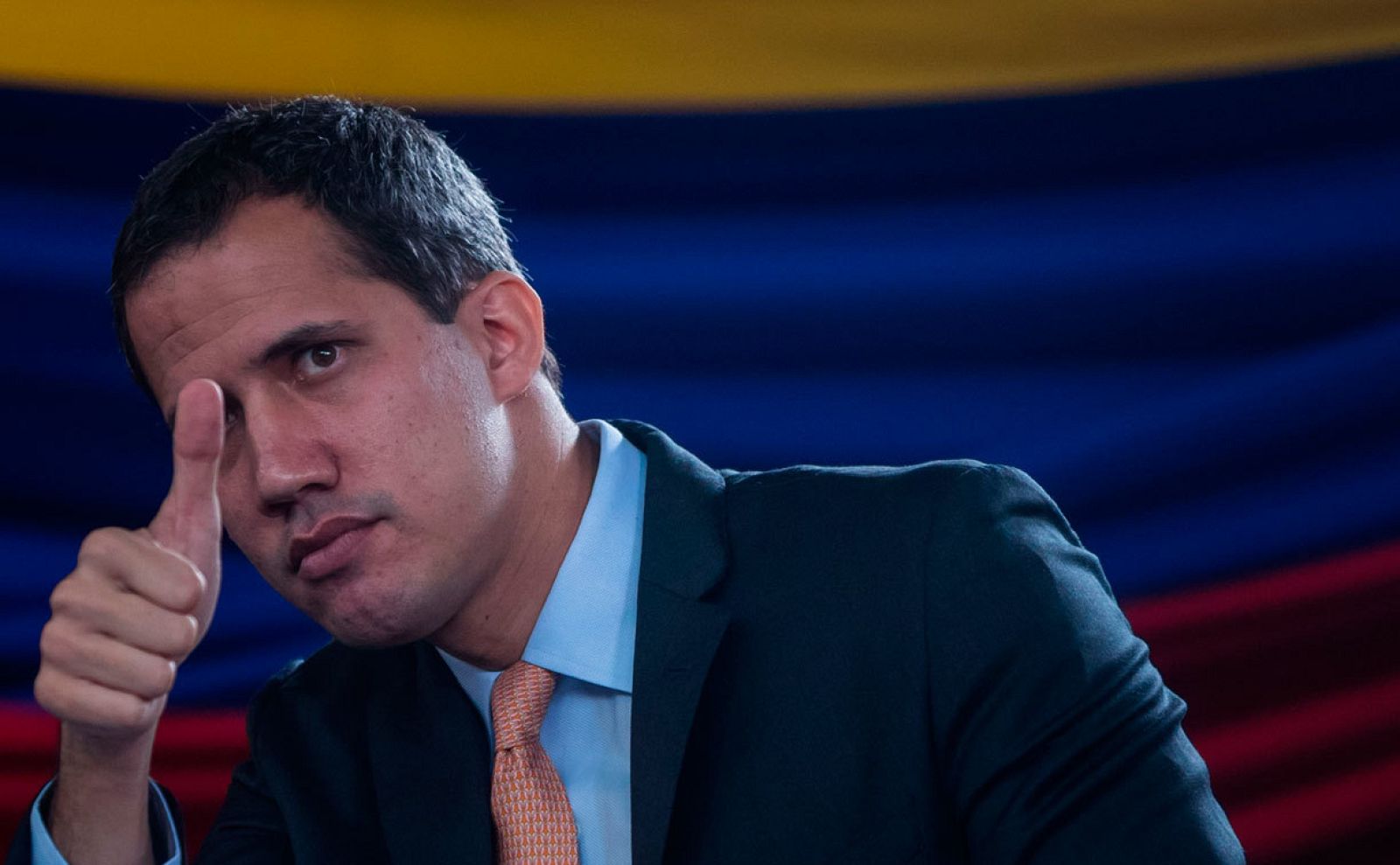Juan Guaidó hace un gesto de aprobación levantando el pulgar con la bandera venezolana detrás.
