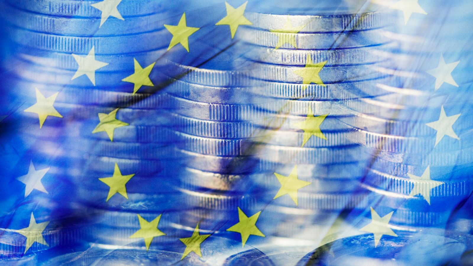 Imagen de archivo de unas monedas de euro junto a una bandera de la Unión Europea