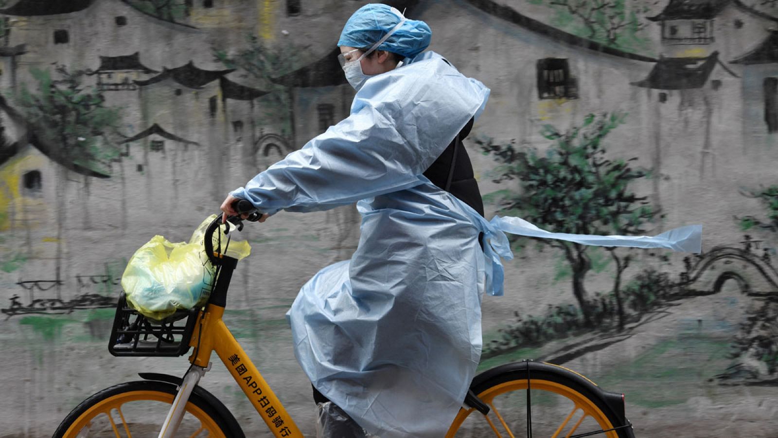 Una mujer con un equipo de protección contra el coronavirus montando en bicicleta por una calle de Wuhan, China.