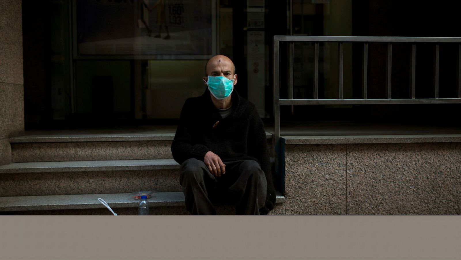 Un hombre con mascarilla sentado en la calle para protegerse del coronavirus.