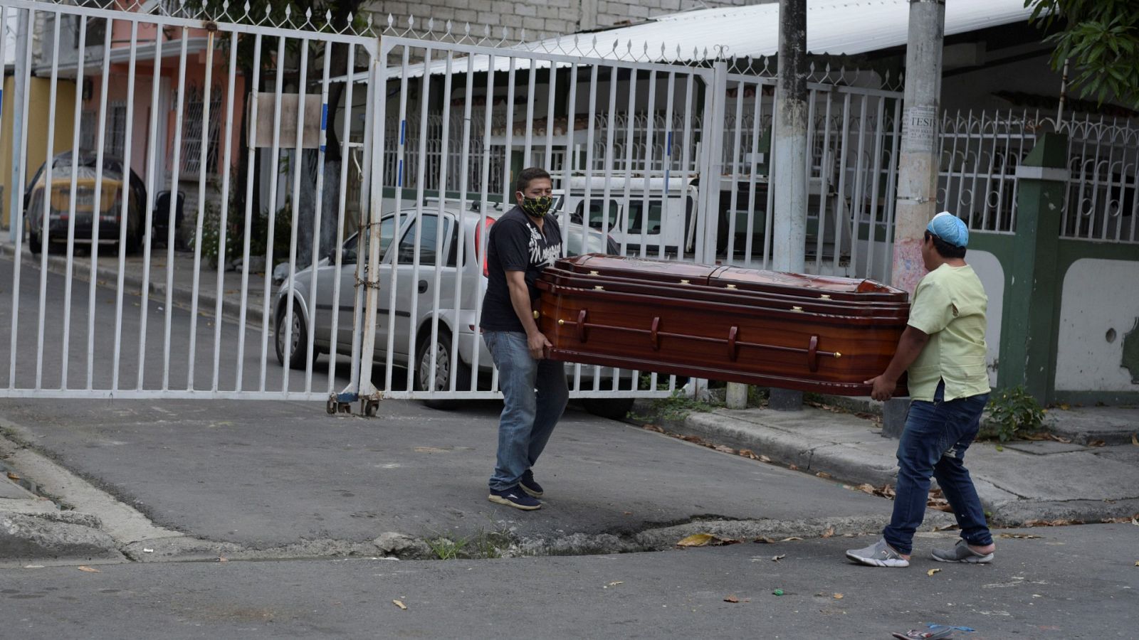 Un familiar y el empleado de una funeraria llevan un ataúd que contiene el cuerpo de una mujer que murió en su casa