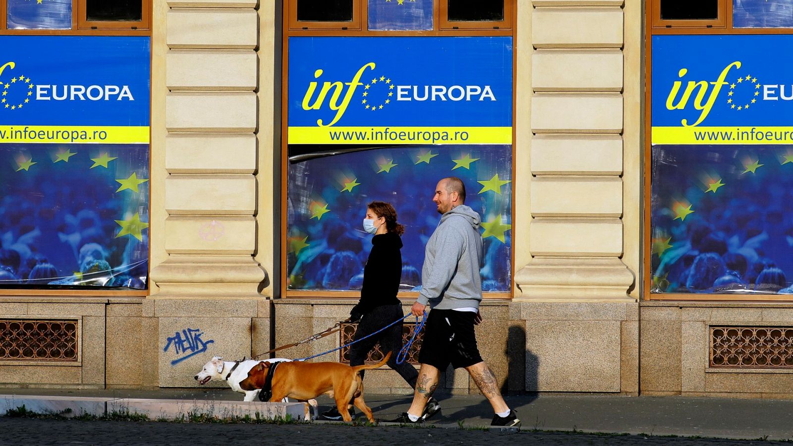 Una pareja pasea con sus perros delante del centro de información de la UE