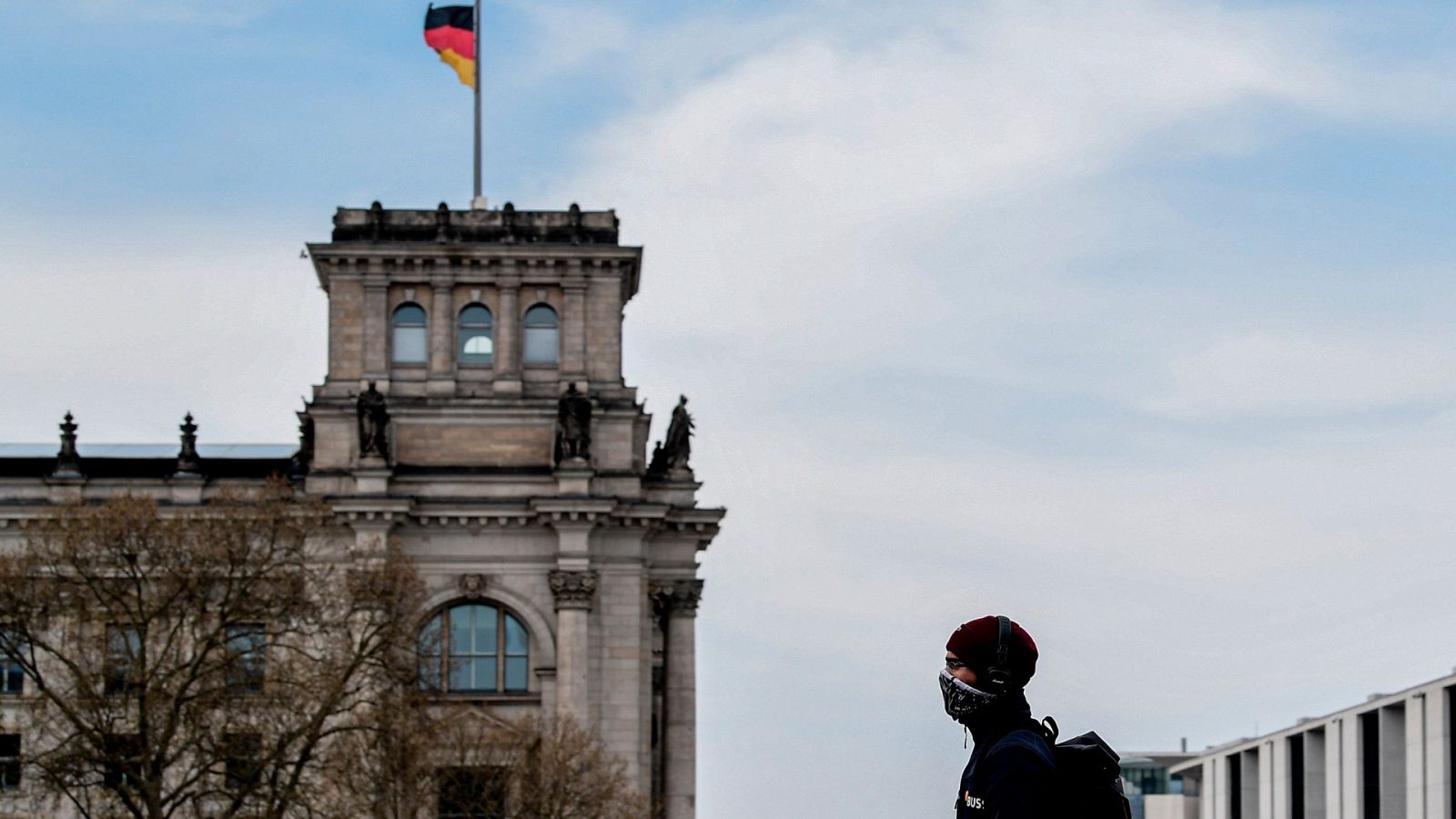 Un hombre con una máscara protectora camina enfrente del Bundestag, el parlamento alemán