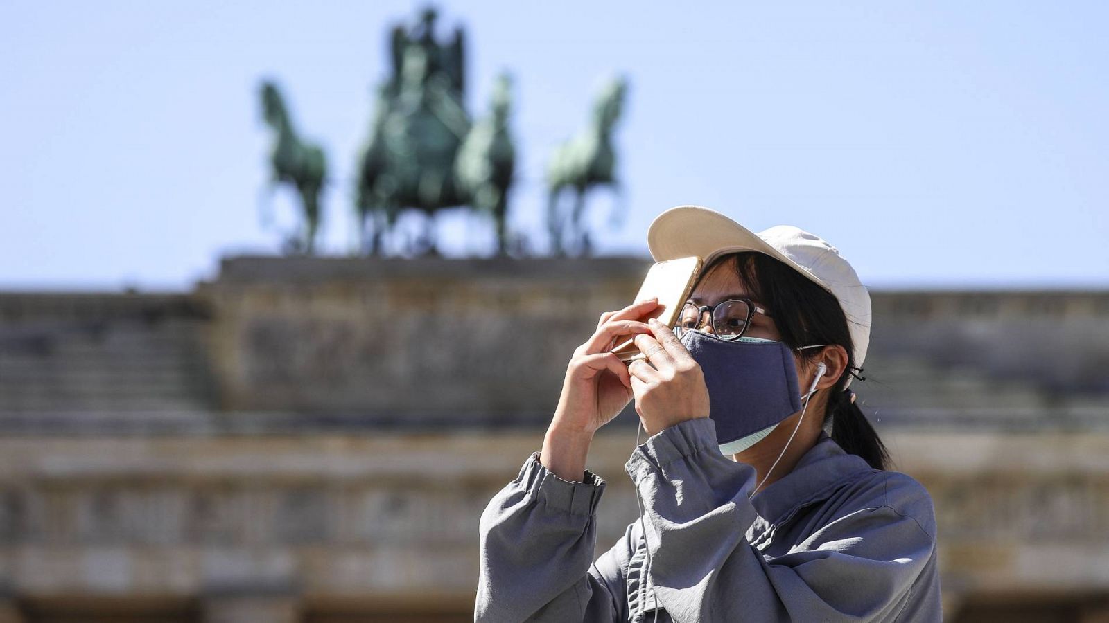 Una turista con mascarilla junto a la puerta de Brandenburgo en Berlín, Alemania
