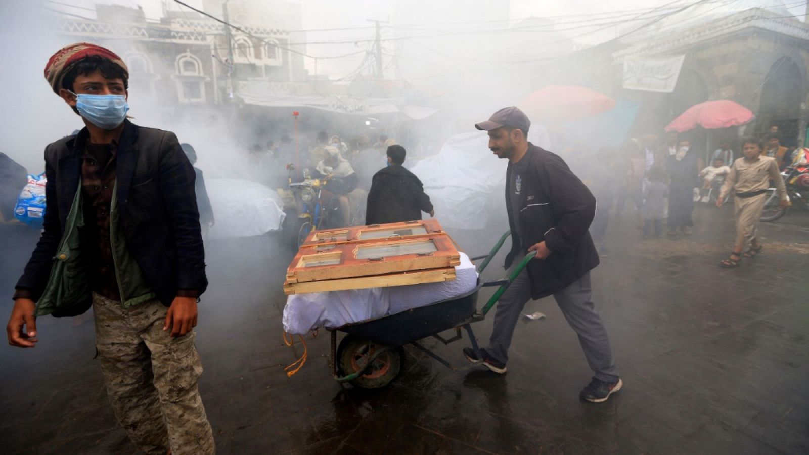 Gente en medio de una nube de sustancia desinfectante utilizada contra el coronavirus en un mercado de Saná, Yemen.