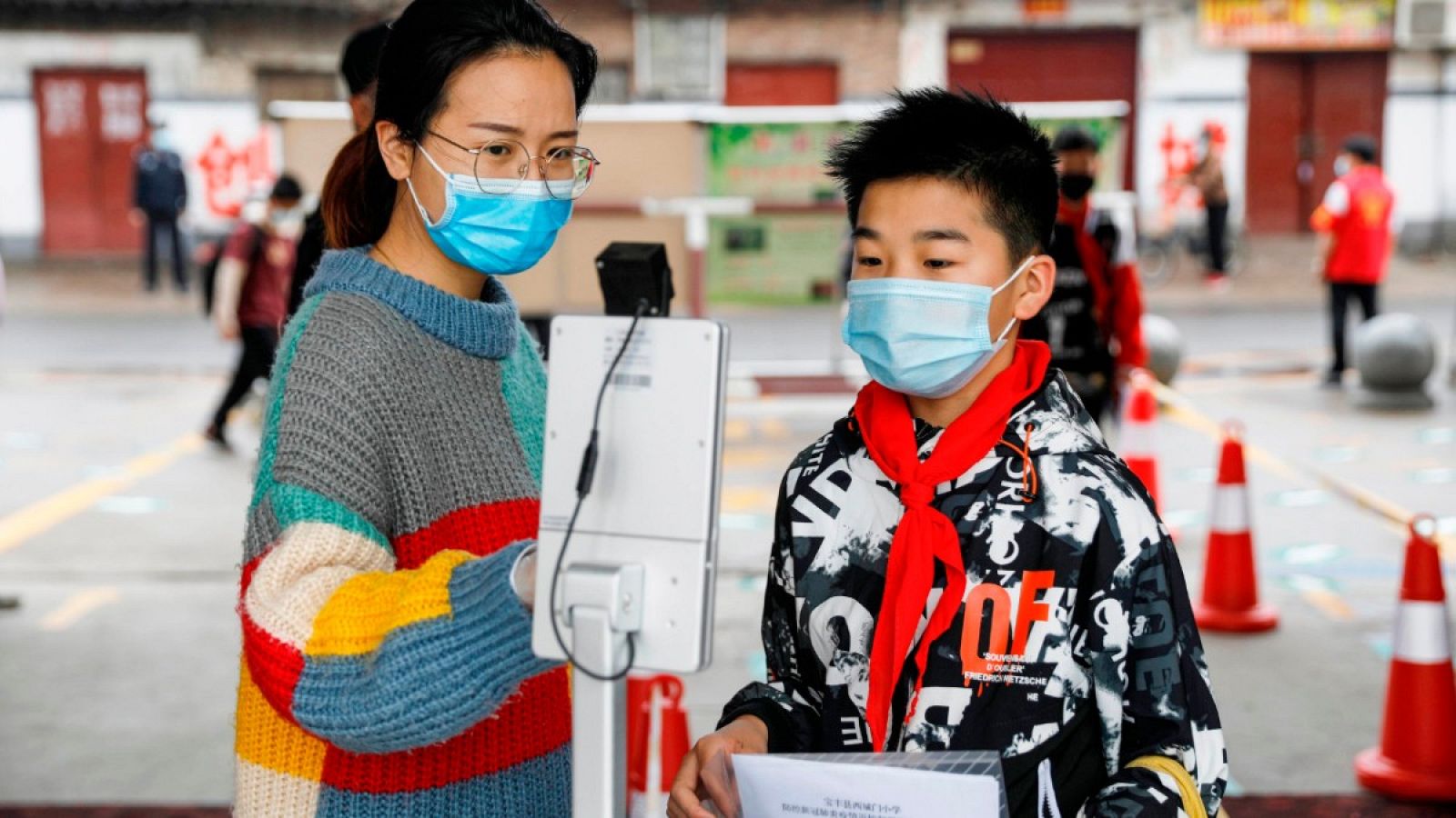 Una persona guía a un estudiante para verificar su temperatura corporal con un escáner térmico antes de ingresar a una escuela primaria en Pingdingshan, China.