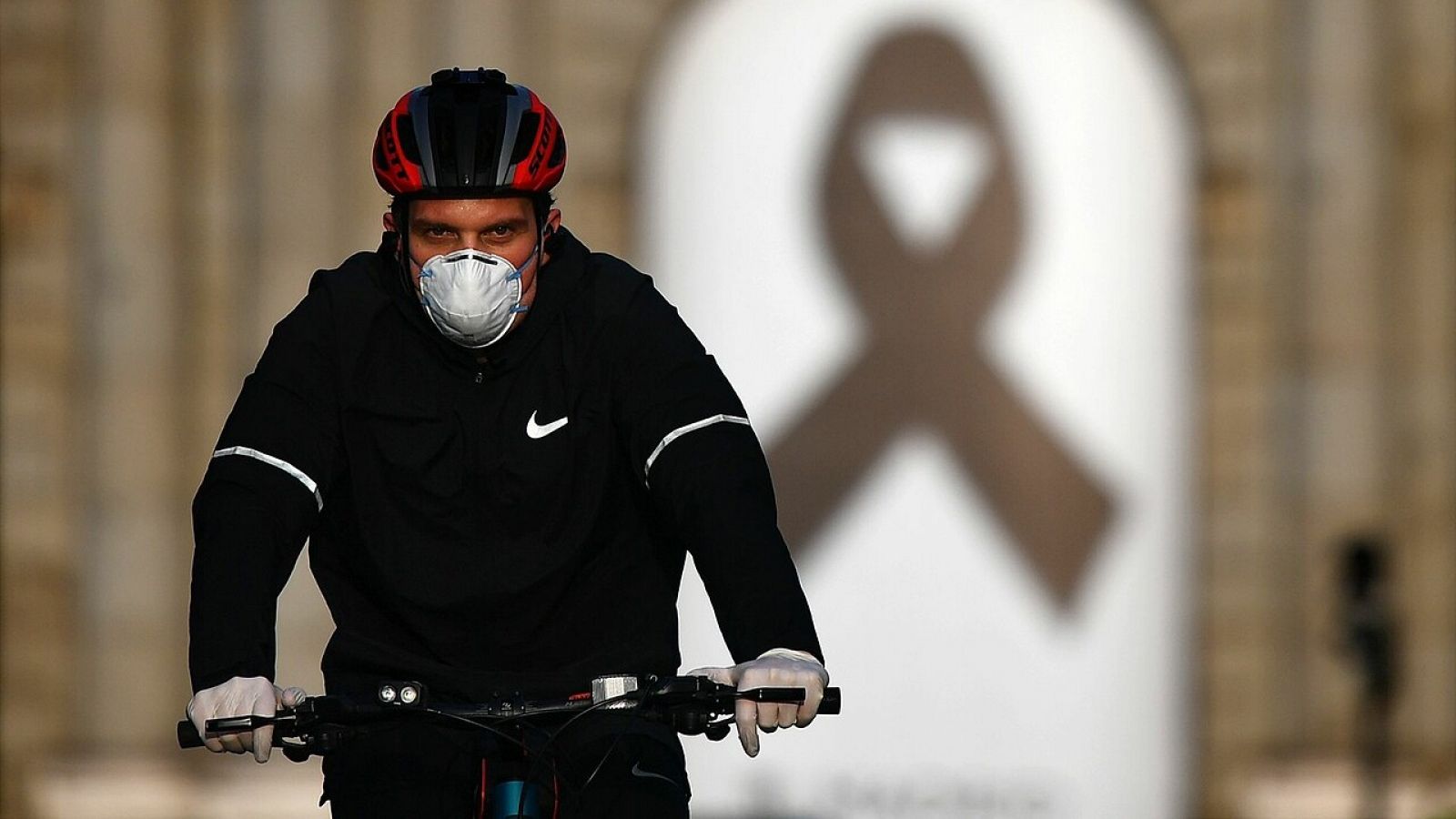 Un ciclista pasa frente a la Puerta de Alcalá, en Madrid, donde se ha colocado un lazo negro como homenaje a las víctimas del coronavirus