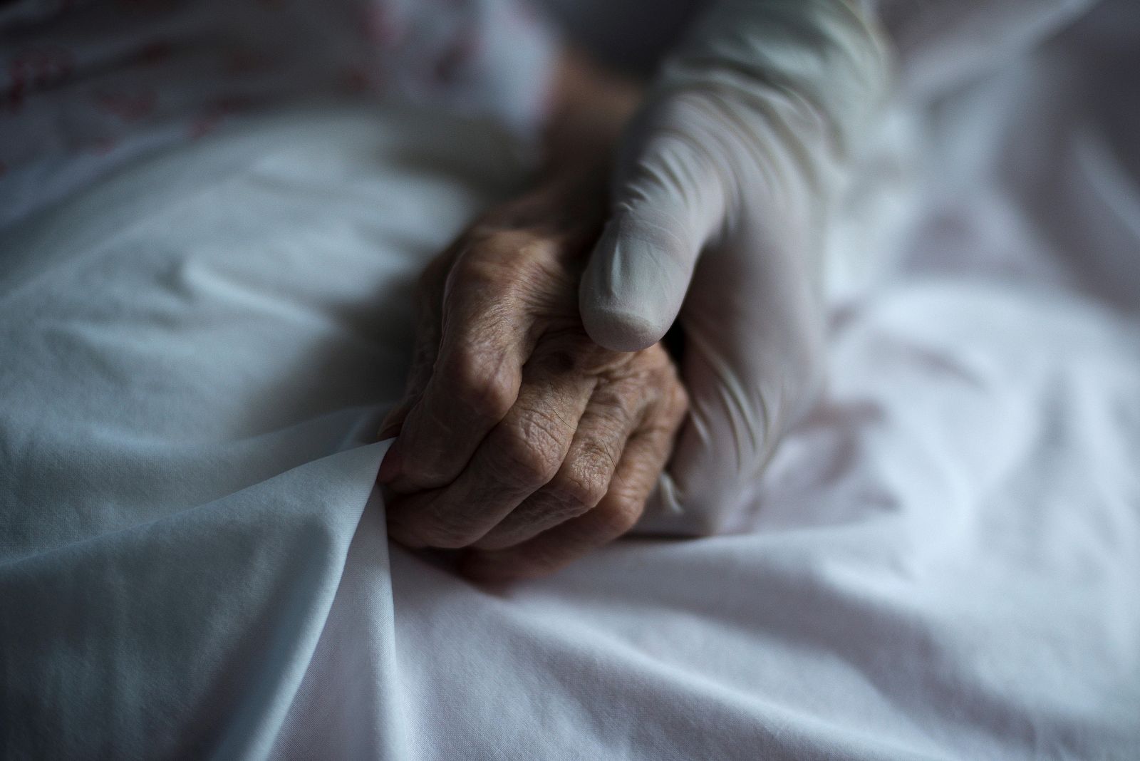 Una trabajadora equipada con guantes sujeta la mano de una residente en un geriátrico