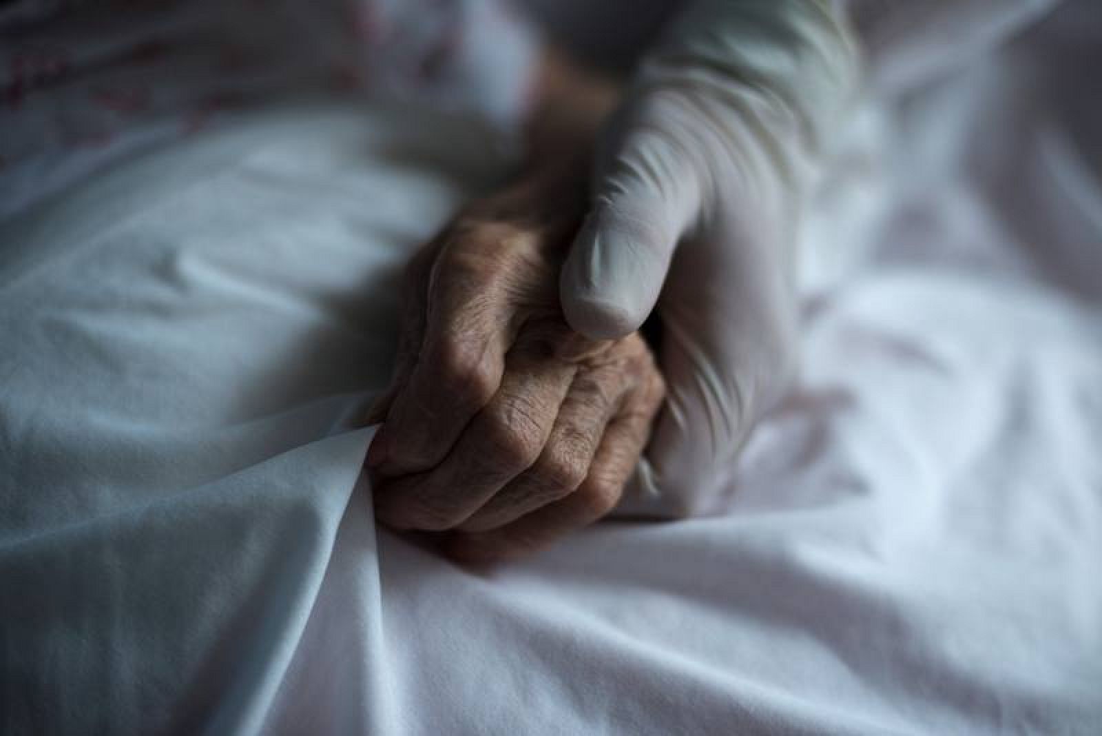 Una trabajadora equipada con guantes sujeta la mano de una residente en un geriátrico