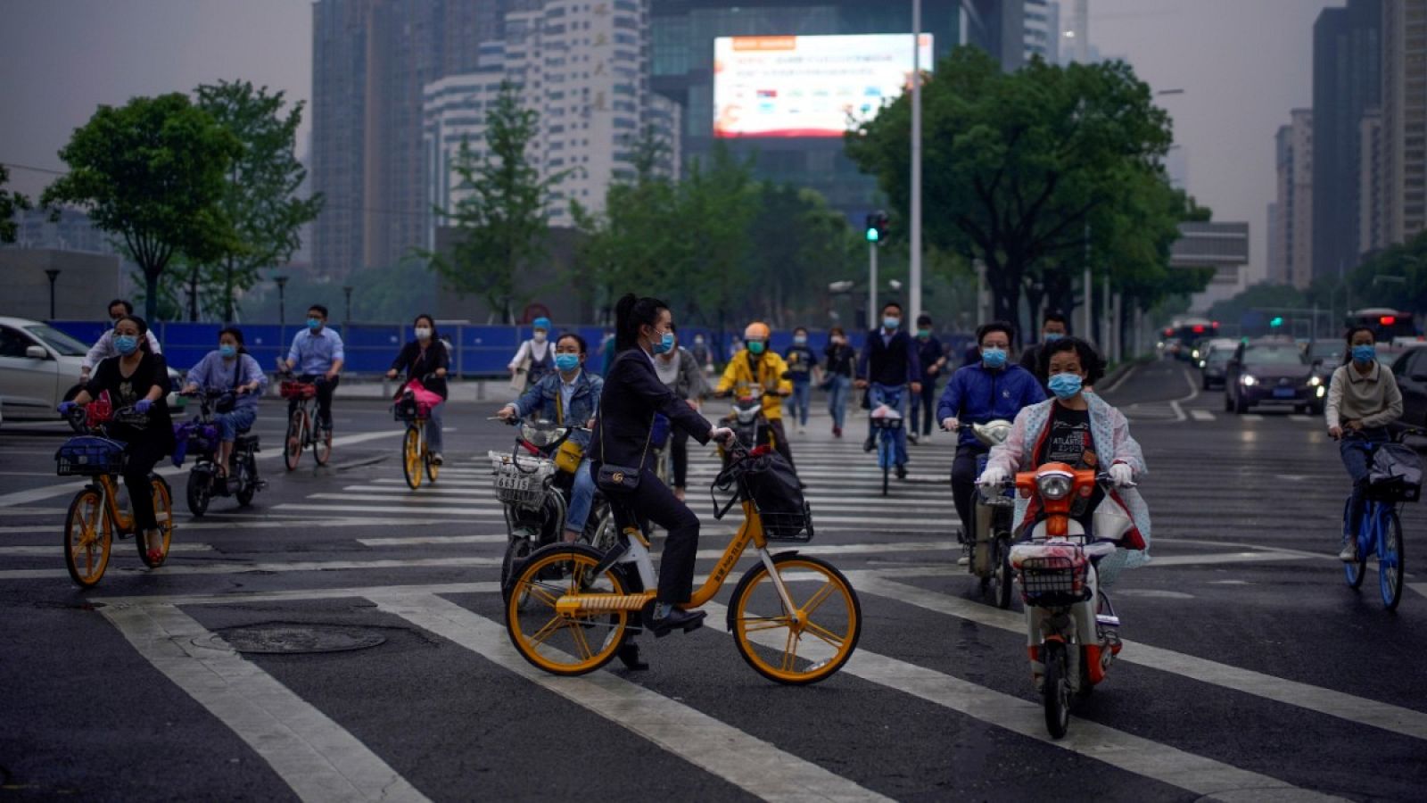 Varias personas con mascarilla desplazándose en moto o en bicicleta por una carretera de Wuhan, China.