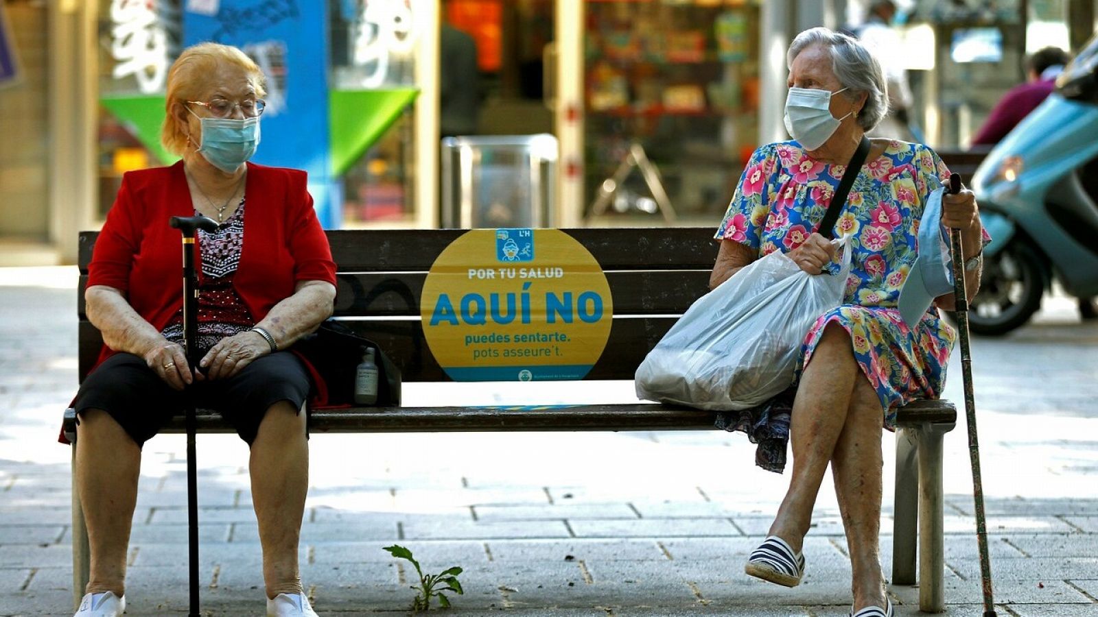 Dos mujeres conversan en un banco de L'Hospitalet (Barcelona) este jueves, cuando ha comenzado la obligatoriedad de llevar mascarilla en todos los espacios públicos. EFE/Toni Albir