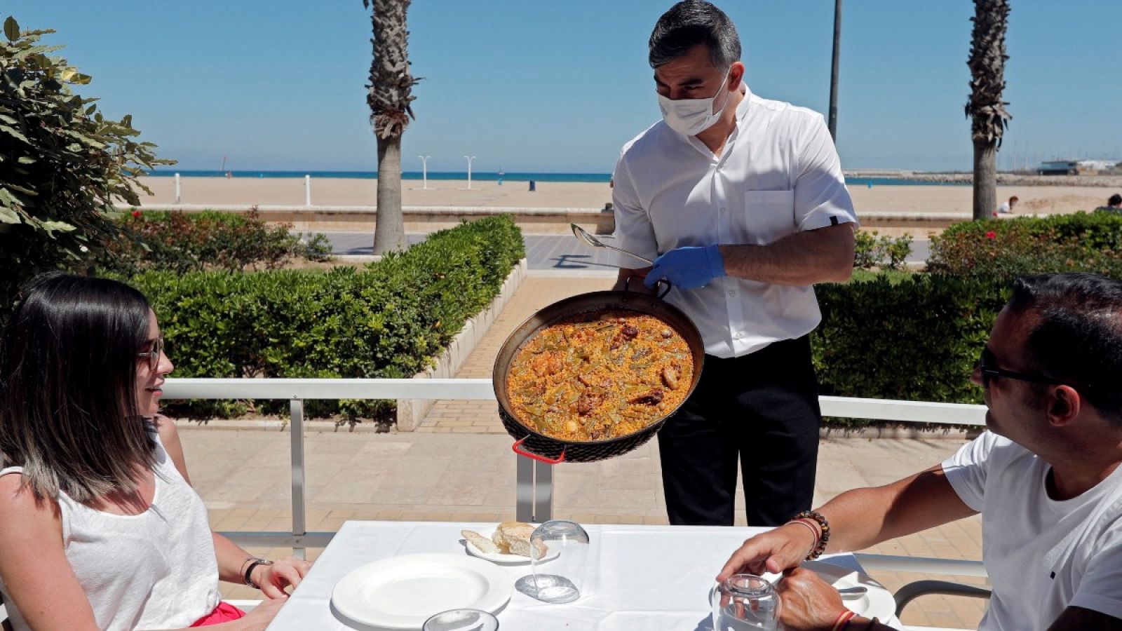 Un camarero sirve una paella en una terraza de un restaurante de la playa de la Malvarrosa de Valencia