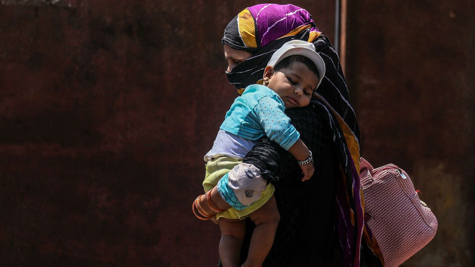 Una mujer carga con su bebe de camino a una estación de tren en Bombay (India).