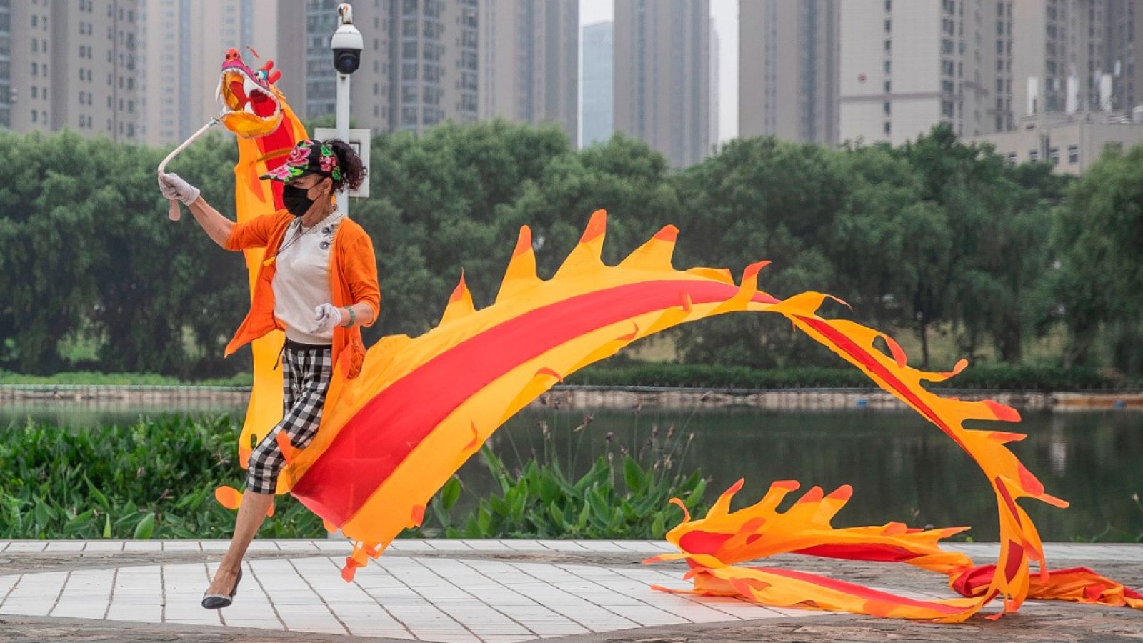 Una mujer con mascarilla sujetando una cinta con forma de dragón en un parque de Wuhan, China.