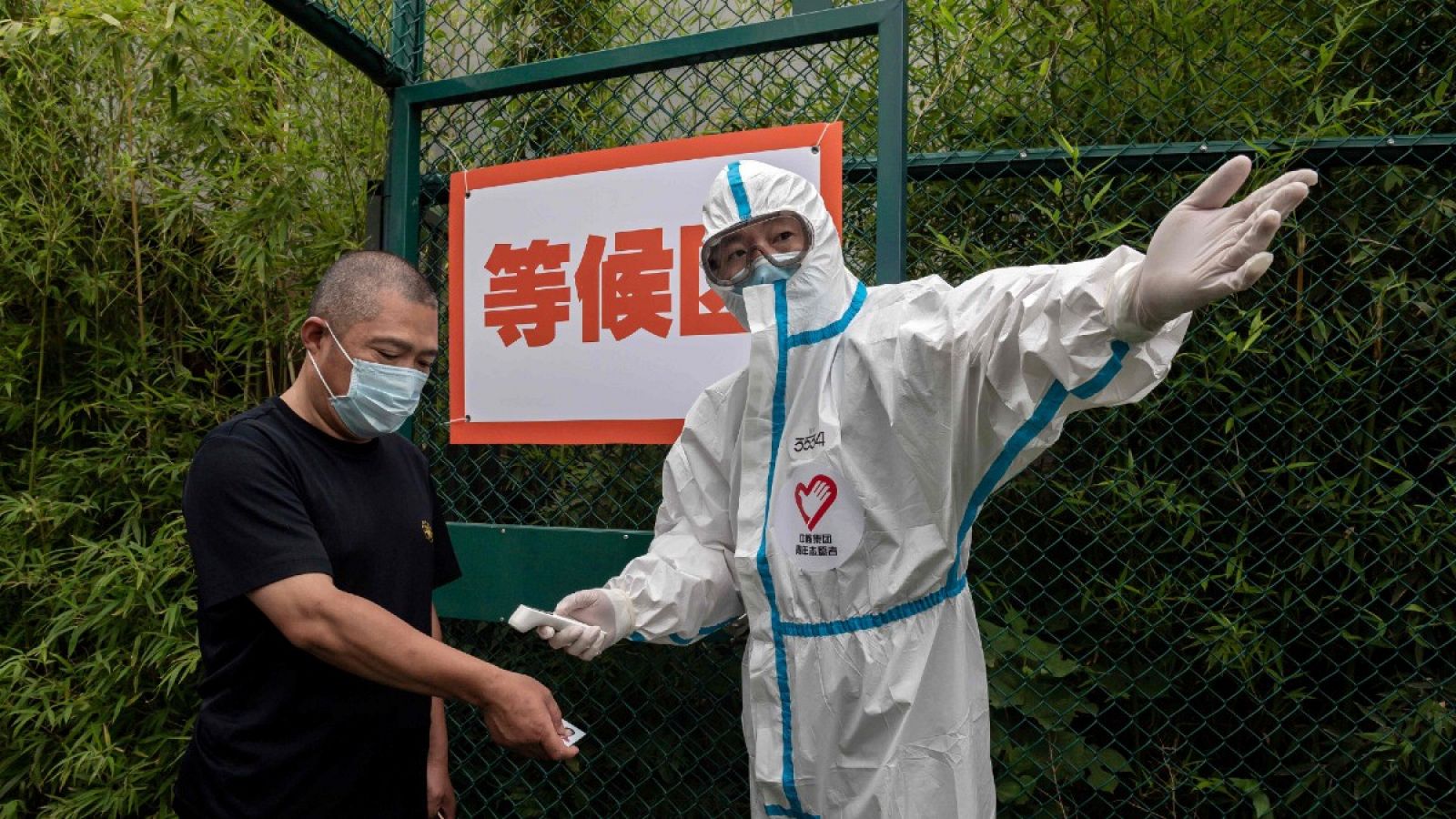 Un hombre con mascarilla se somete a un control de temperatura corporal por un trabajador sanitario vestido con un equipo de protección personal en Pekín