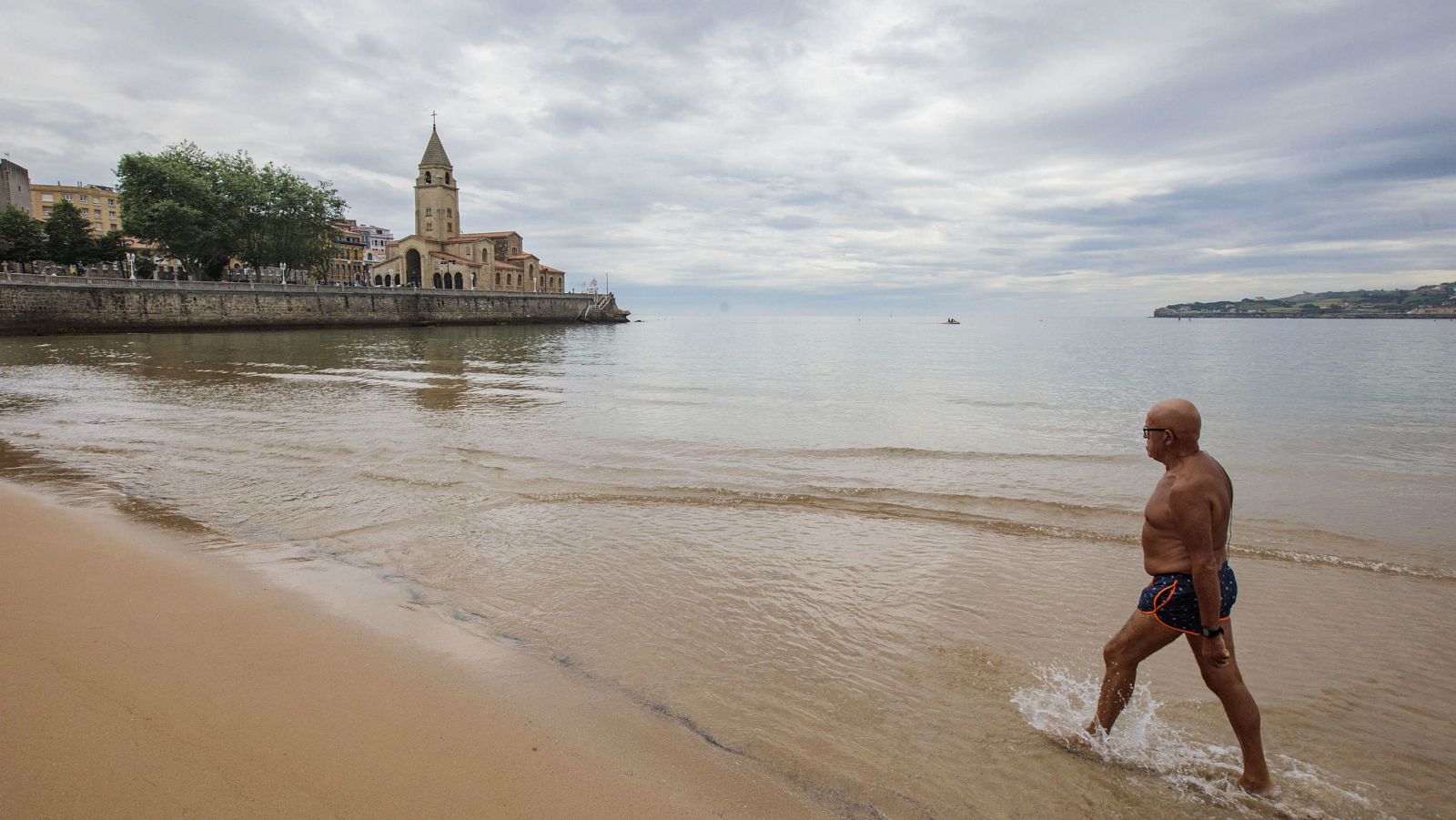 Un hombre avanza por la playa de San Lorenzo de Gijón, vacía en un día nublado y dejando atrás la fase dura del confinamiento en España.