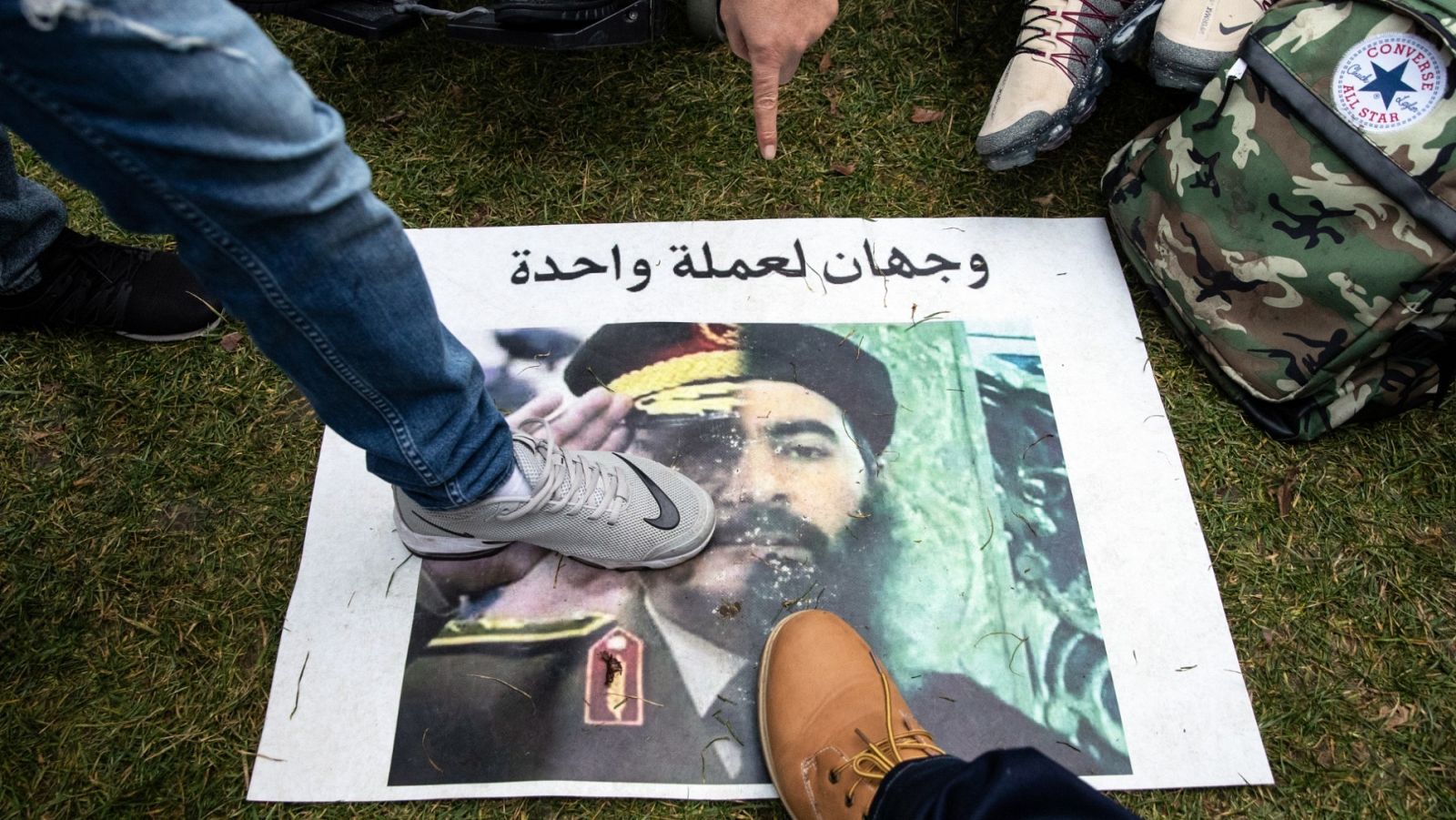 Varias personas pisan una pancarta con un retrato con una mitad del mariscal National Army Khalifa Haftar y el líder del ISIS Abu Bakr al-Baghdadi con la frase "Dos caras de la misma moneda". 
