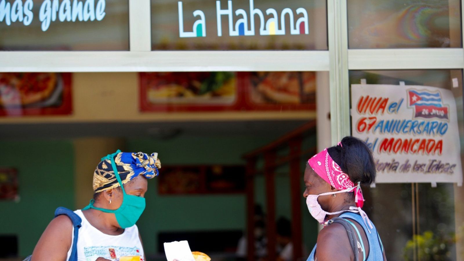 Dos mujeres con mascarilla hablando en la entrada de una cafetería en La Habana, Cuba.