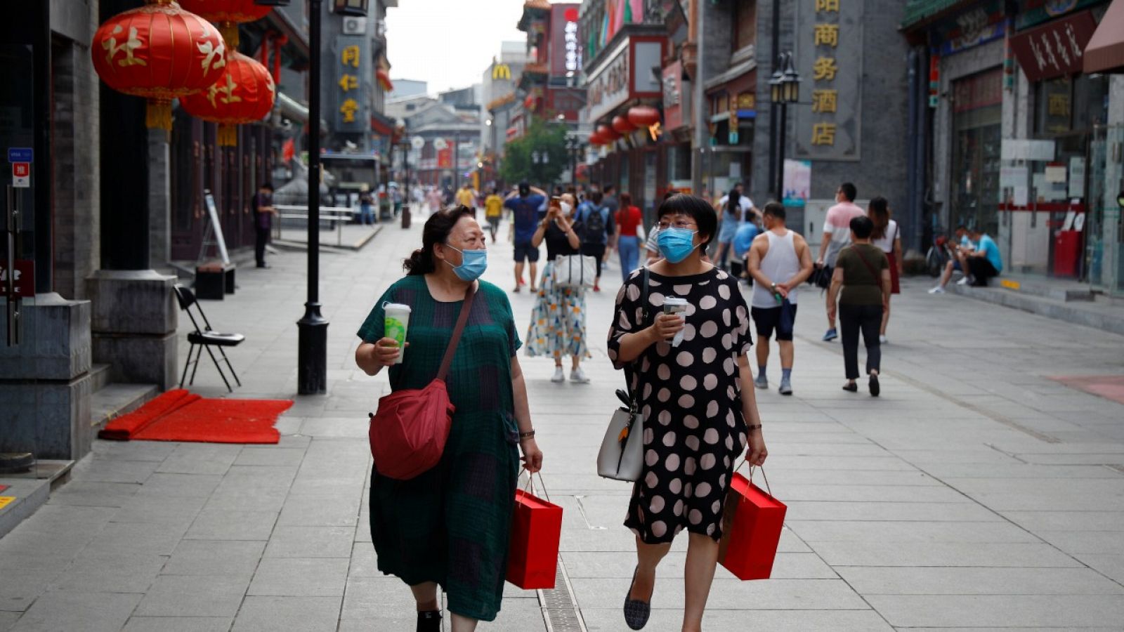 Dos mujeres con mascarilla conversan mientras caminan por una calle comercial de Pekín.